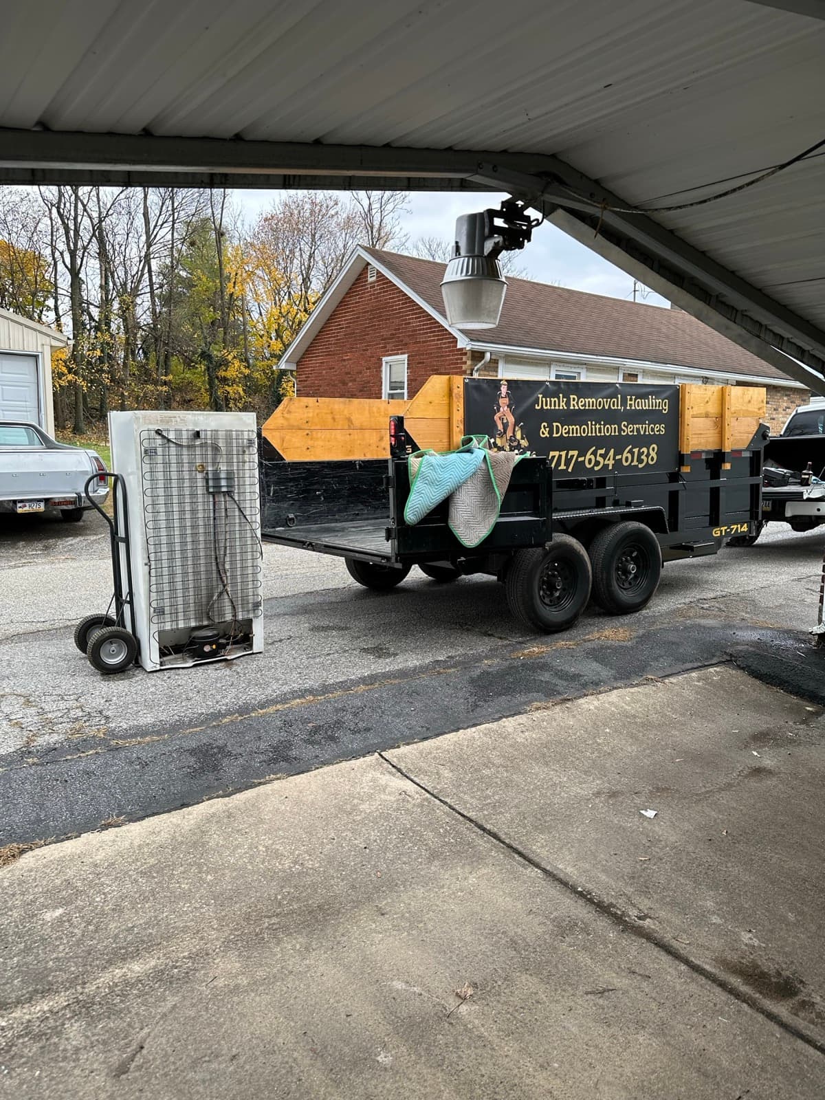 Refrigerator laid on its back with condenser coils exposed beside the branded dump trailer — The Junk Lord, York County PA