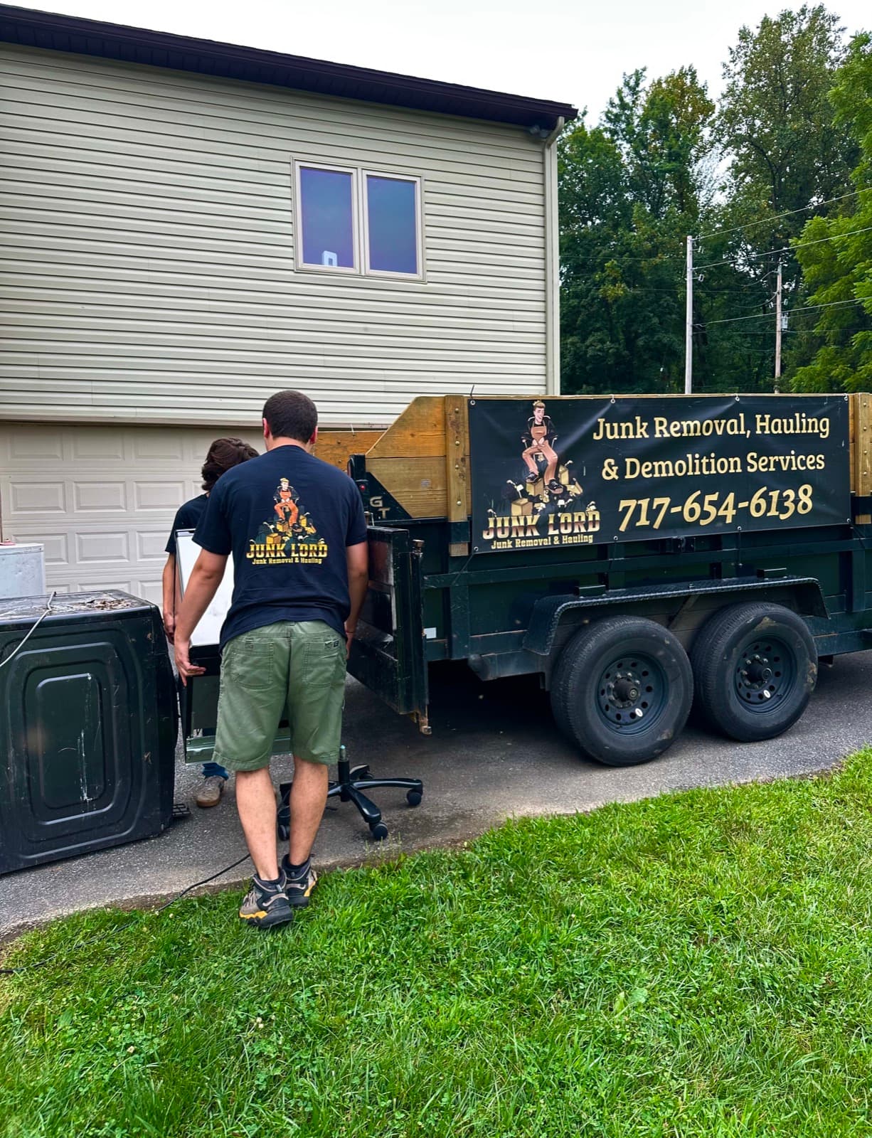 Two Junk Lord crew members carrying a dryer beside the branded dump trailer at a York County, PA home