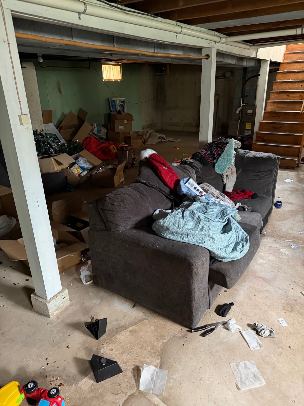 York County basement walkthrough — couch buried under blankets and clothing, scattered Christmas debris across the concrete floor