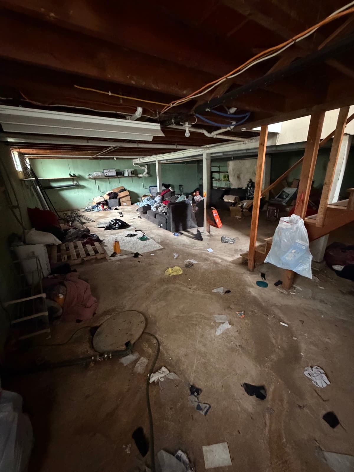 Same York County basement partway through The Junk Lord cleanout — wide debris cleared from the floor but couch, bedding, and boxes still staged at the back wall