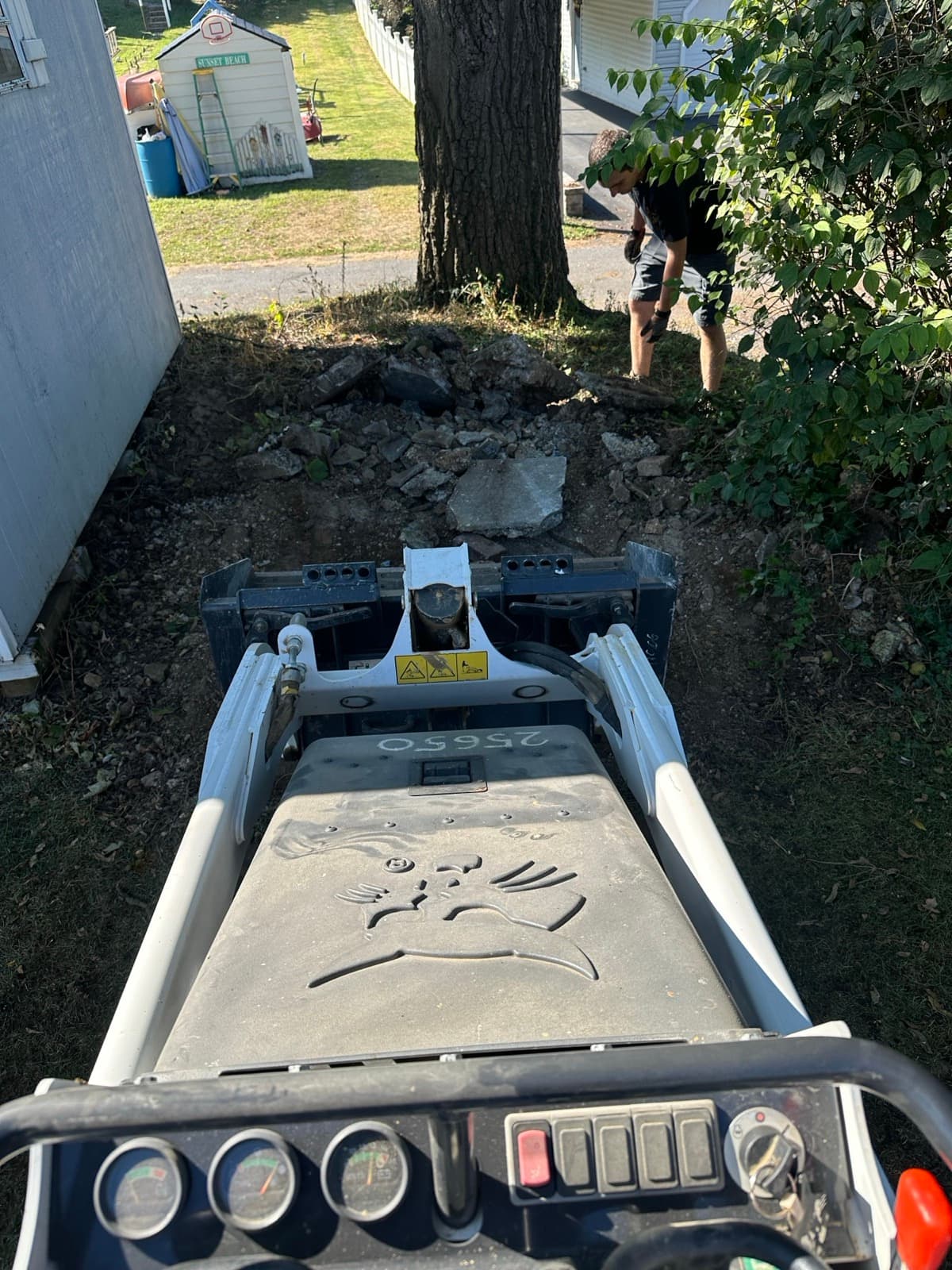 Skid steer excavating concrete and earth during a yard cleanup — The Junk Lord