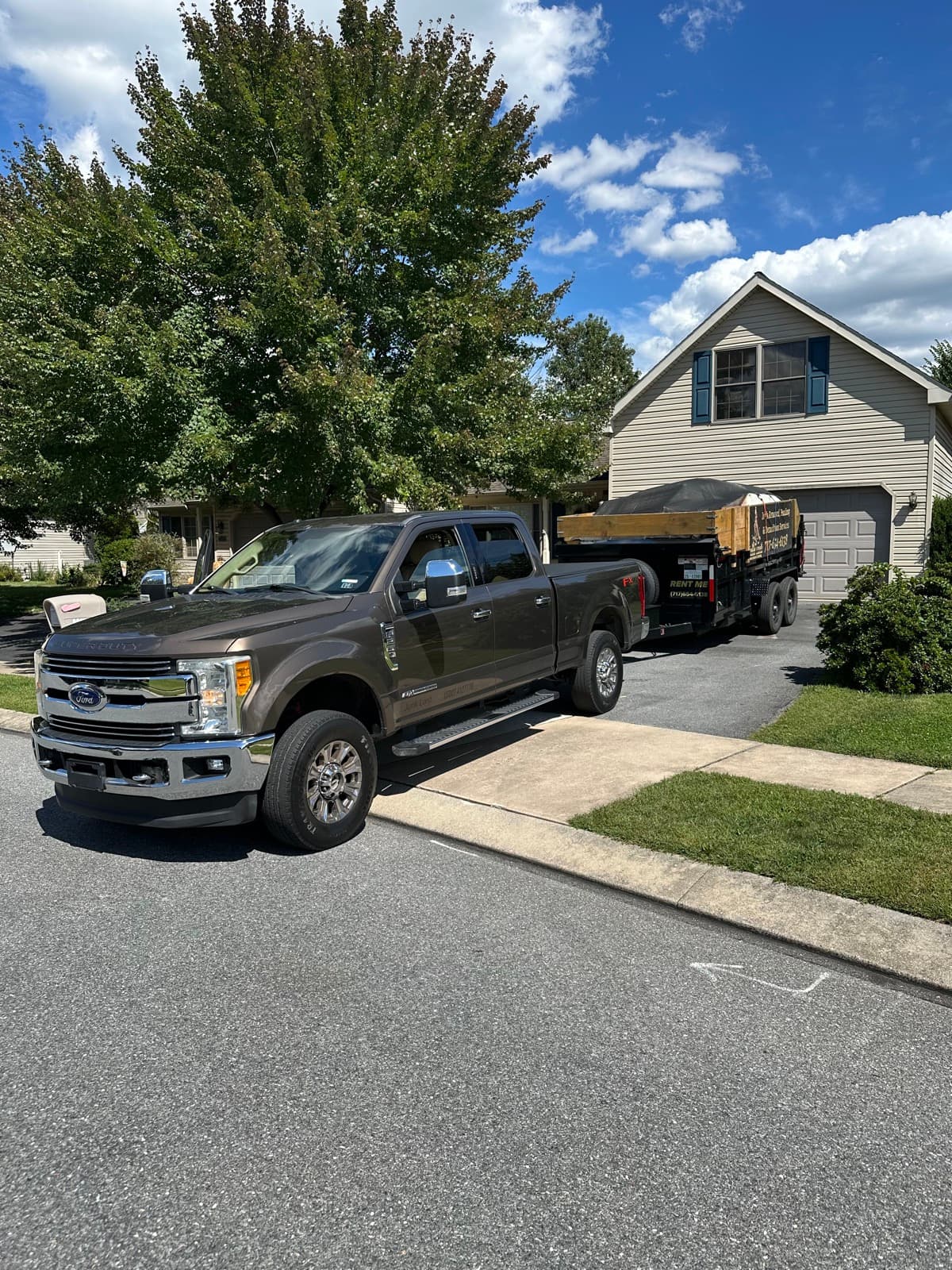 Junk Lord pickup pulling a dump trailer up a sunny driveway for a customer rental drop