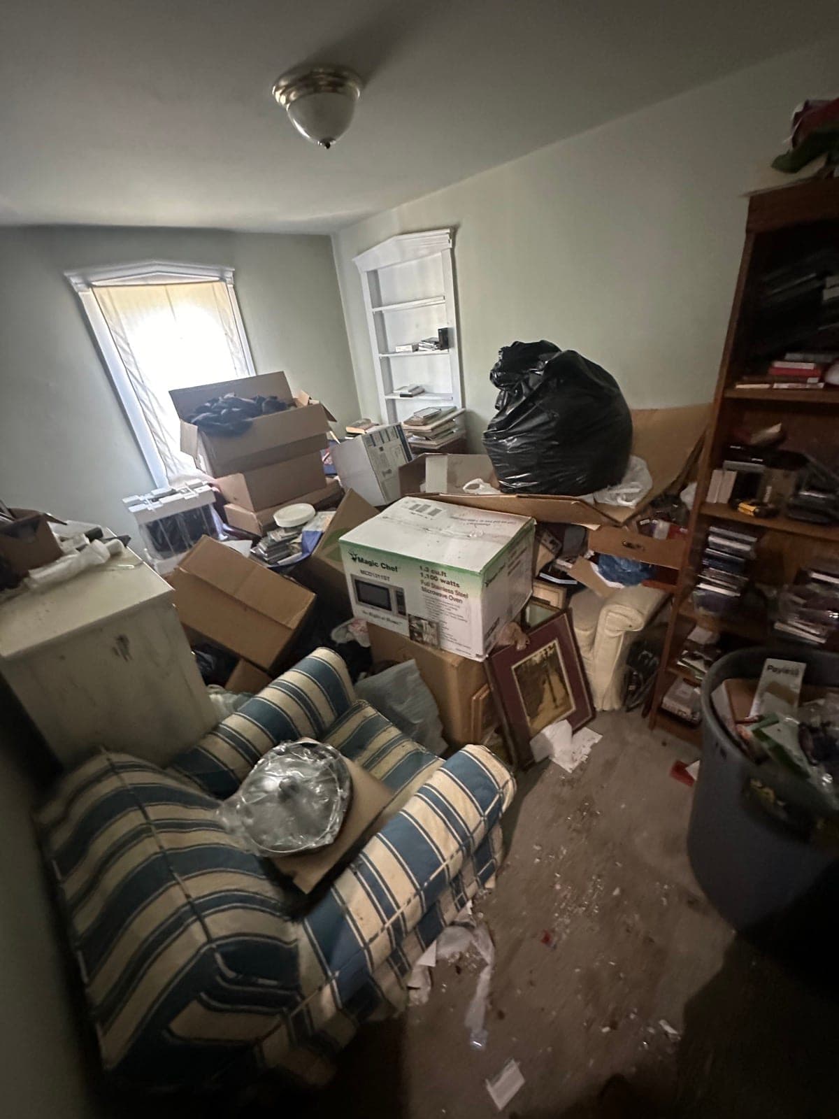Estate cleanout living room with packed bookshelves, a striped sofa, and household goods boxed for sort-and-haul