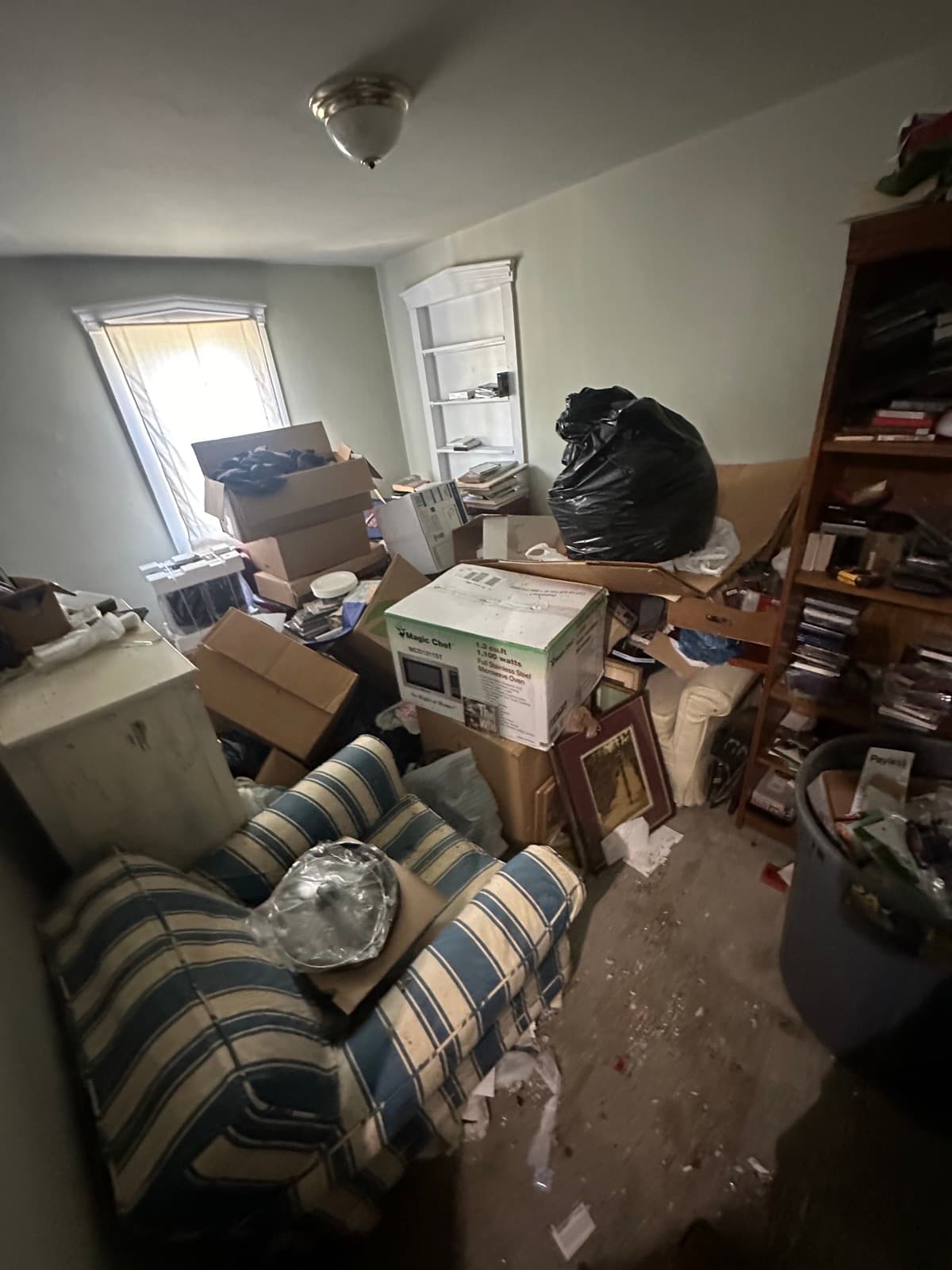 Estate cleanout living room with packed bookshelves, a striped sofa, and household goods boxed for sort-and-haul