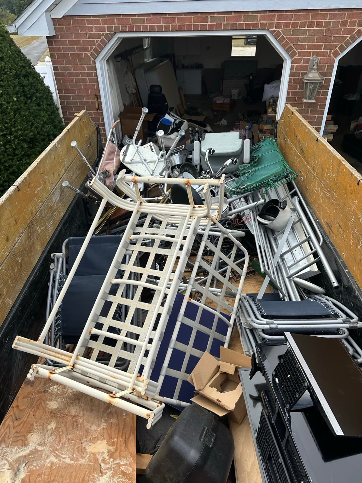 Patio lounge frames, lawn chairs, a step ladder, and a flat-screen TV loaded in the trailer — The Junk Lord