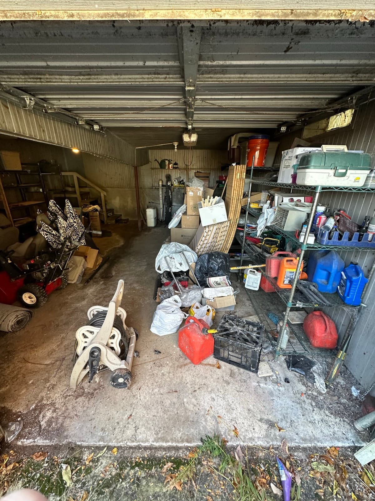 Red and blue gas cans, wire shelving, and a hose reel packed into a metal shed — The Junk Lord, York County PA