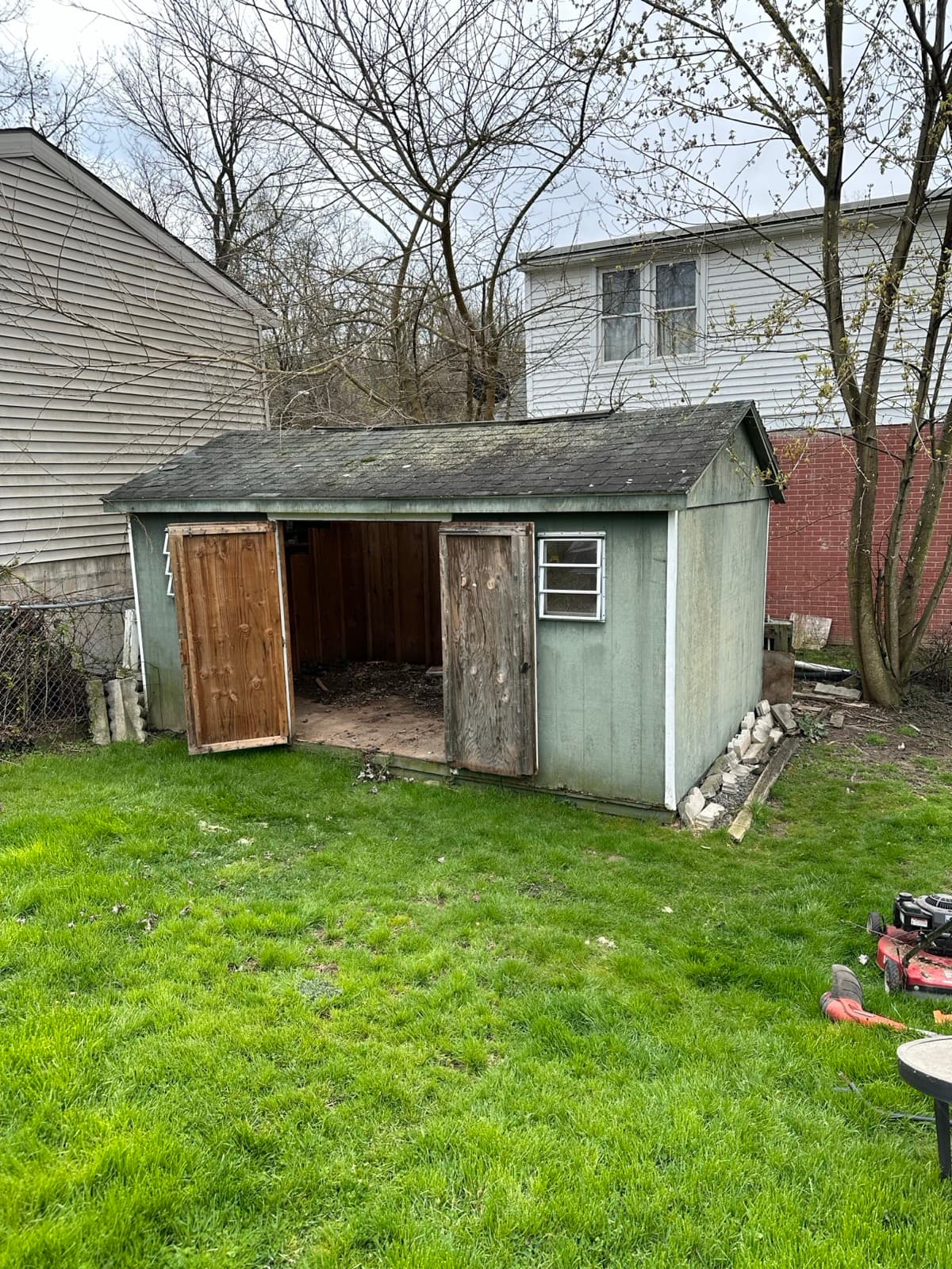 Green wooden shed with both doors open on an emptied dirt floor — The Junk Lord
