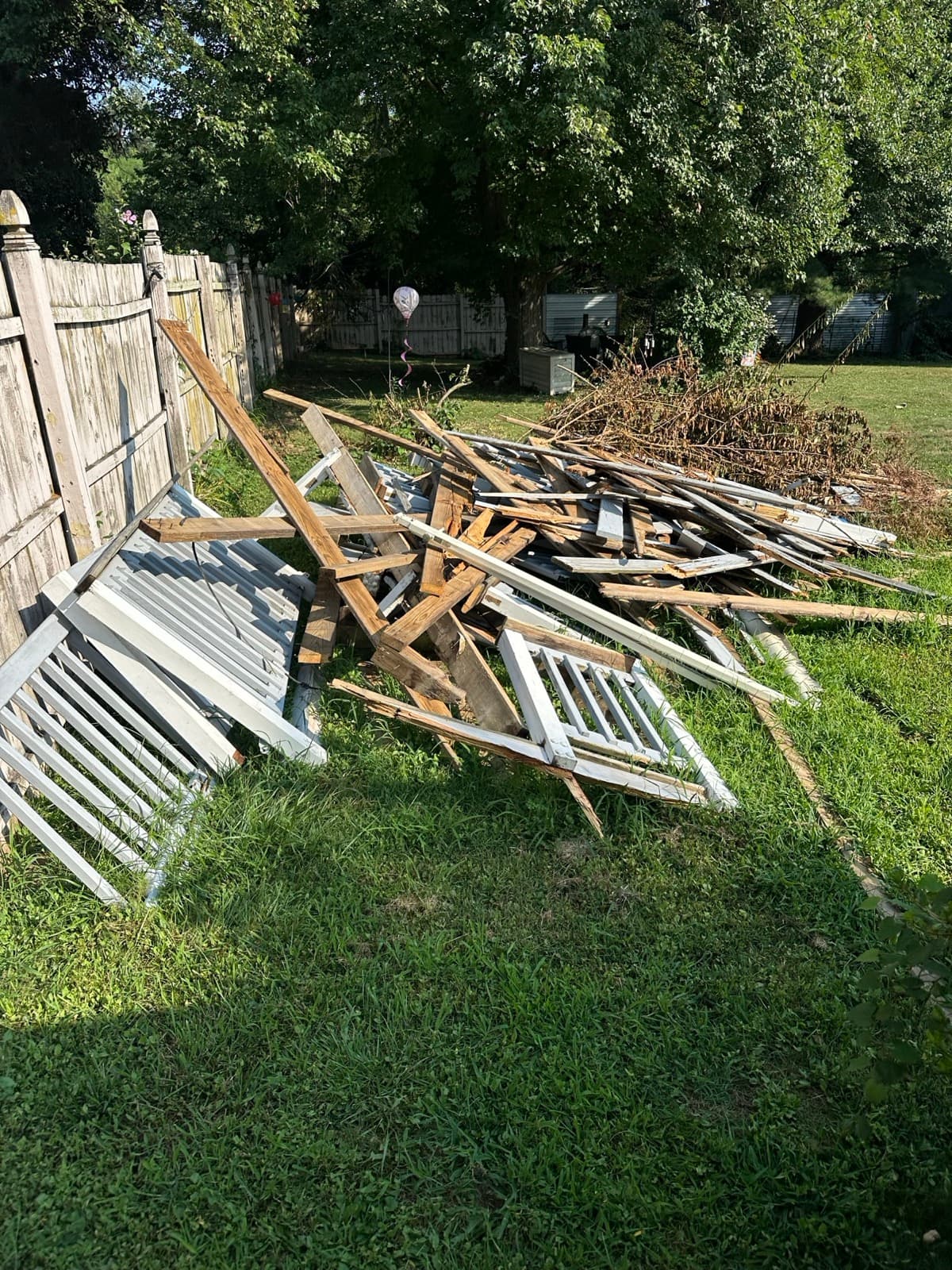 Pile of white porch railings, lattice, and framing lumber in the grass by a deck — The Junk Lord, York County PA