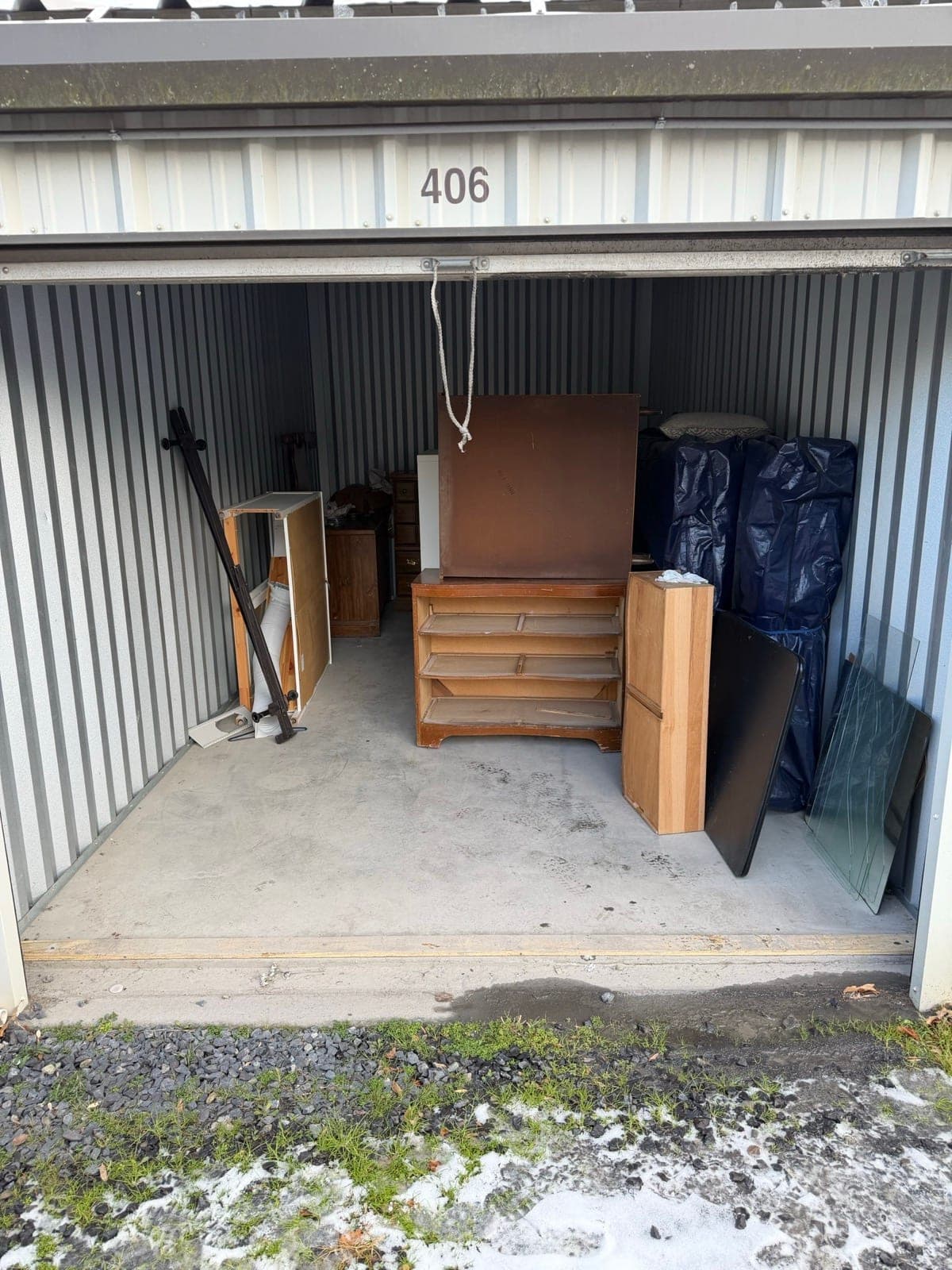 Storage unit #406 holding a stripped dresser, tarp-wrapped bundles, and a table frame — The Junk Lord