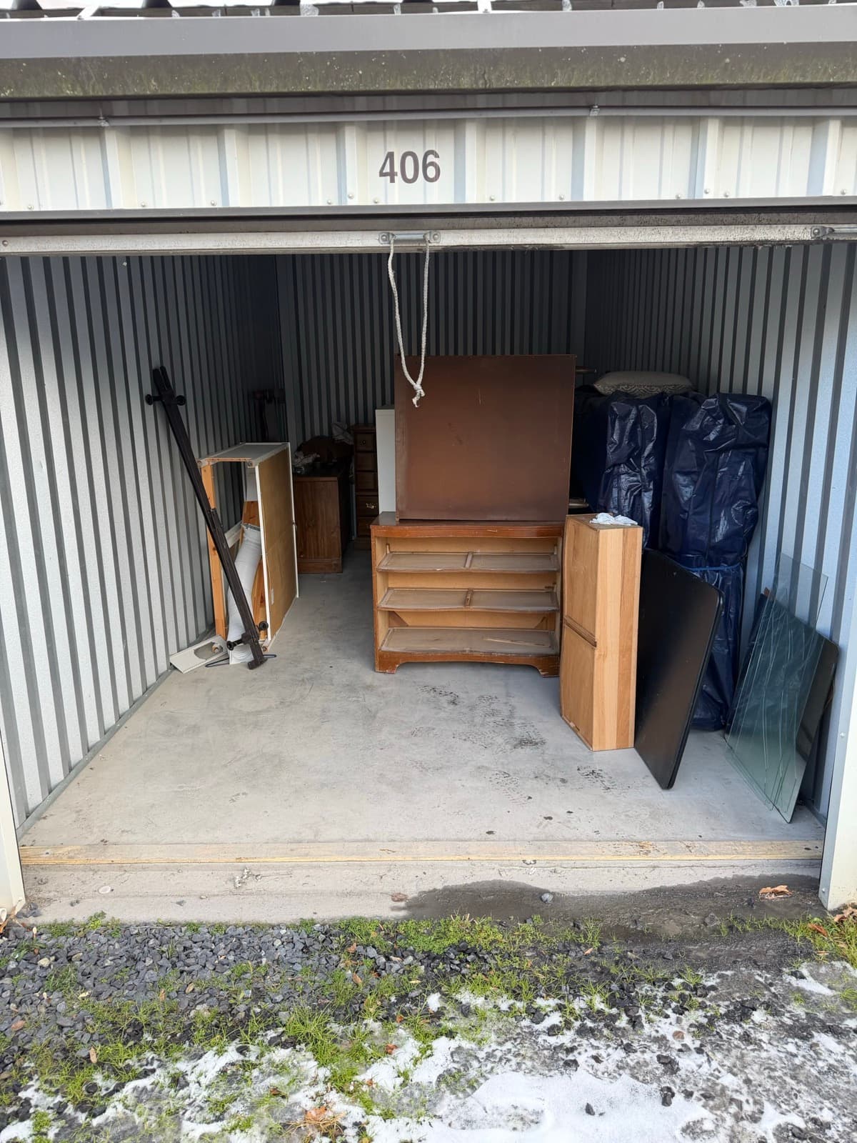 Storage unit #406 holding a stripped dresser, tarp-wrapped bundles, and a table frame — The Junk Lord