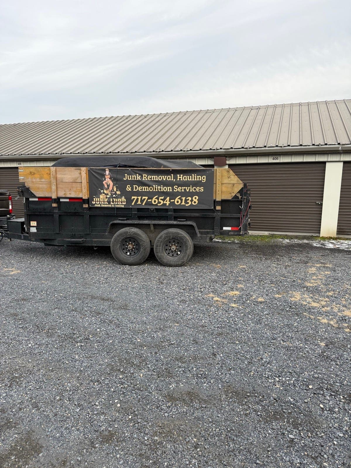 Tarped branded dump trailer parked on the gravel outside storage unit 406 — The Junk Lord