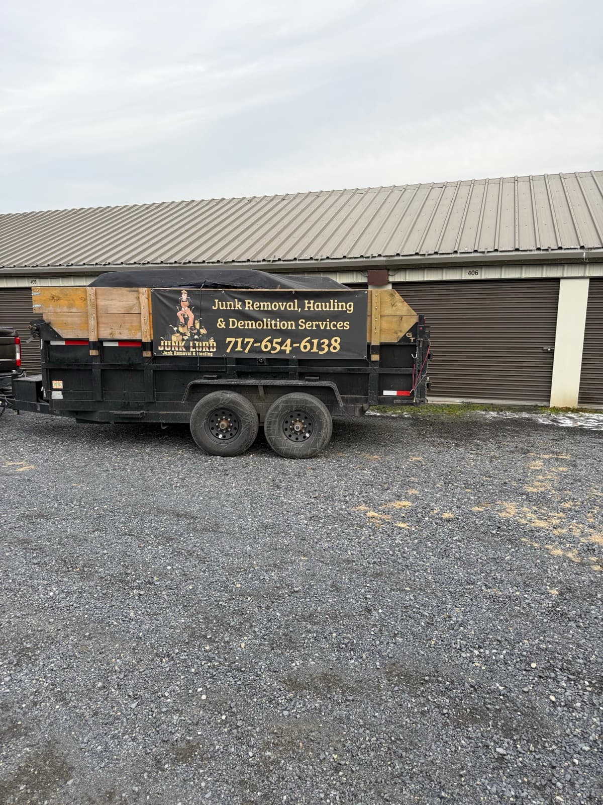 Tarped branded dump trailer parked on the gravel outside storage unit 406 — The Junk Lord